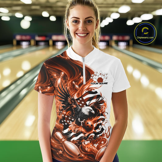 Front view of a female model in a bowling lane wearing a white and orange quarter zip shirt with eagle artwork and flowing flag inspired accents.