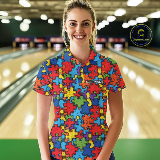 A woman stands in a bowling alley wearing a short-sleeve poloshirt covered in a colorful jigsaw puzzle pattern. The shirt has a custom name printed on the chest