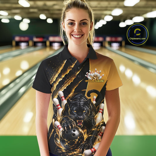 A woman wearing a custom bowling-themed short-sleeve polo shirt with a black and gold design featuring a panther, bowling pins, and a bowling ball graphic. The background shows a blurred bowling alley with lanes and lights.