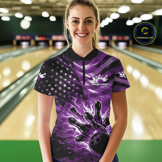 Female model wearing a black bowling quarter-zip shirt at the lane featuring purple flame bowling artwork and flag-inspired details.