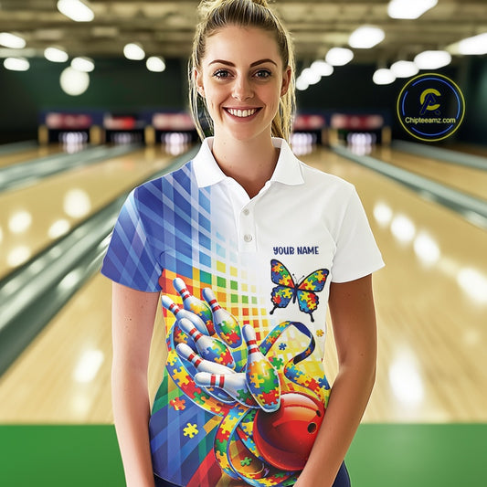 Female model in a bowling alley, front view wearing white and blue polo shirt featuring puzzle butterfly bowling artwork and ribbon accents