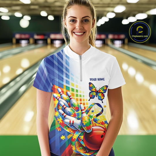 Female model in a bowling lane wearing a white and blue quarter-zip shirt, puzzle butterfly and bowling ribbon artwork with soft colorful accents.