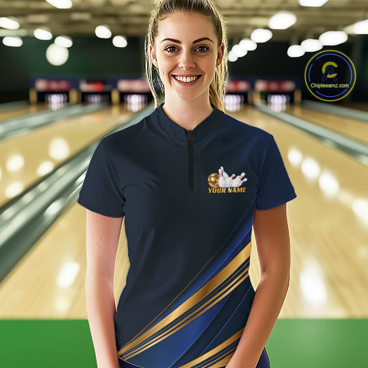 A woman stands in a bowling alley wearing a navy blue short-sleeve bowling shirt with gold and blue diagonal stripes and a small custom graphic on the chest. The background shows blurred bowling lanes, and a circular 'Championship.
