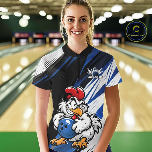A woman stands in a bowling alley wearing a custom printed short-sleeve bowling shirt. The shirt features a black and blue striped design with white diagonal accents, a cartoon rooster holding a blue bowling ball, and a customizable name graphic.
