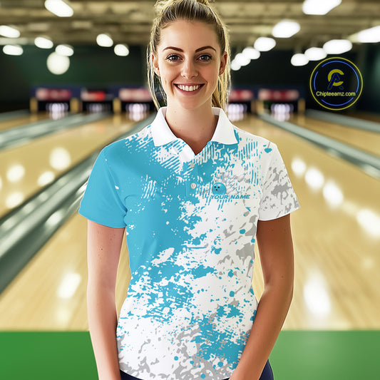 Female model front view at bowling lane wearing white polo shirt with teal blue and white splatter pattern, sporty bowling venue scene
