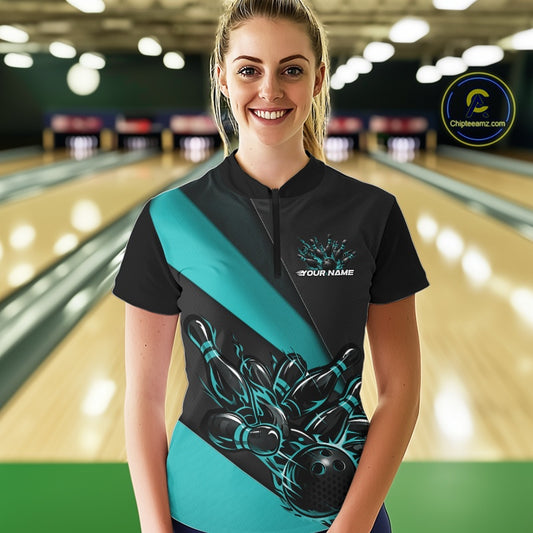 Female model front view inside bowling center wearing black and turquoise blue quarter zip shirt with flame bowling strike artwork