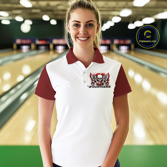 A woman stands in a bowling alley wearing a bowling shirt with polo collar, red skull-themed bowling graphic with black wings, pins, bowling ball