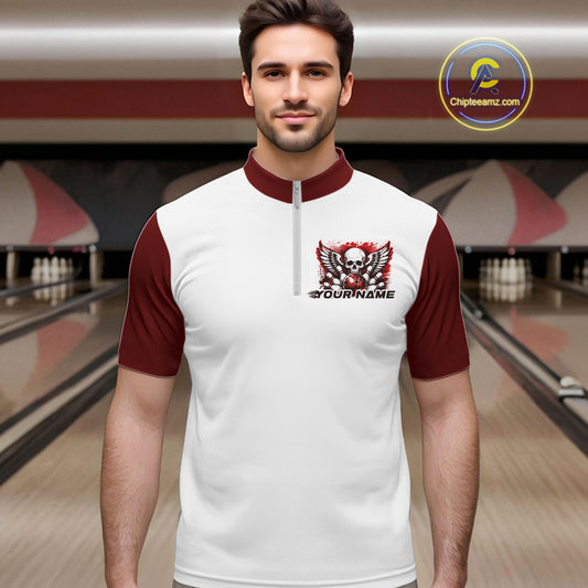 A man stands in a bowling alley wearing a bowling shirt with quarter zip collar, red skull-themed bowling graphic with black wings, pins, bowling ball