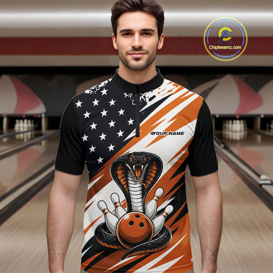 A man stands in a bowling alley wearing a black, white, and orange bowling shirt with stars, diagonal stripes, a cobra, pins, and an orange ball.