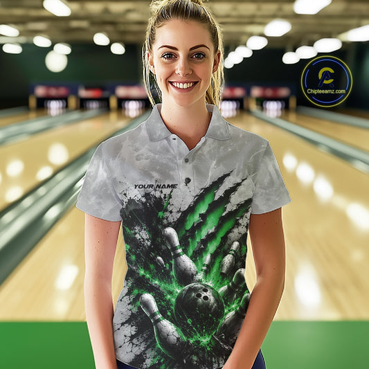 Front view of a female model wearing a gray bowling polo shirt showcasing a dramatic green bowling ball and pins graphic with claw-mark artwork at a bowling lane.