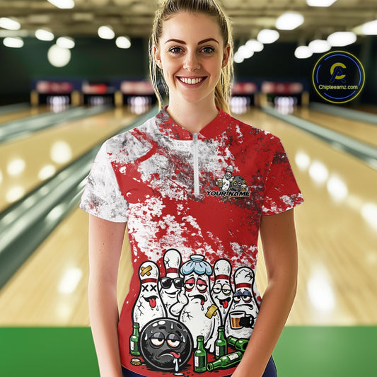 Front view of a female model in a bowling lane wearing a red and white grunge splatter bowling quarter-zip shirt, featuring playful cartoon bowling pins and beer bottle graphics.