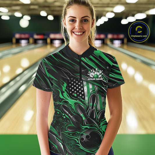 Female model in a bowling alley wearing black and green quarter zip shirt, front view featuring patriotic flaming bowling ball hitting pins dynamic artwork