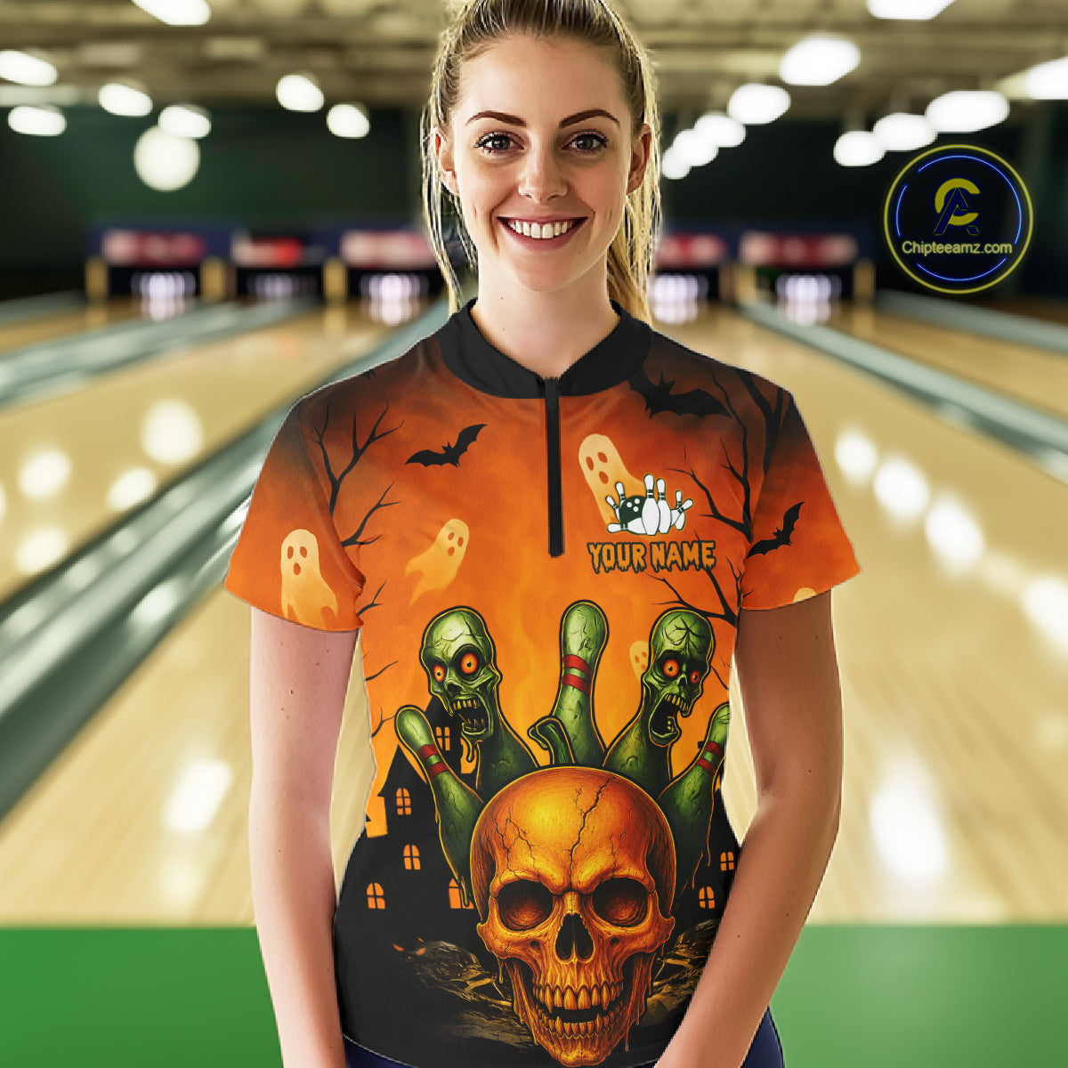 A woman wearing a short-sleeve Halloween bowling-themed t-shirt with a skull, ghosts, and green fingers design, standing in front of a blurred bowling alley background. 