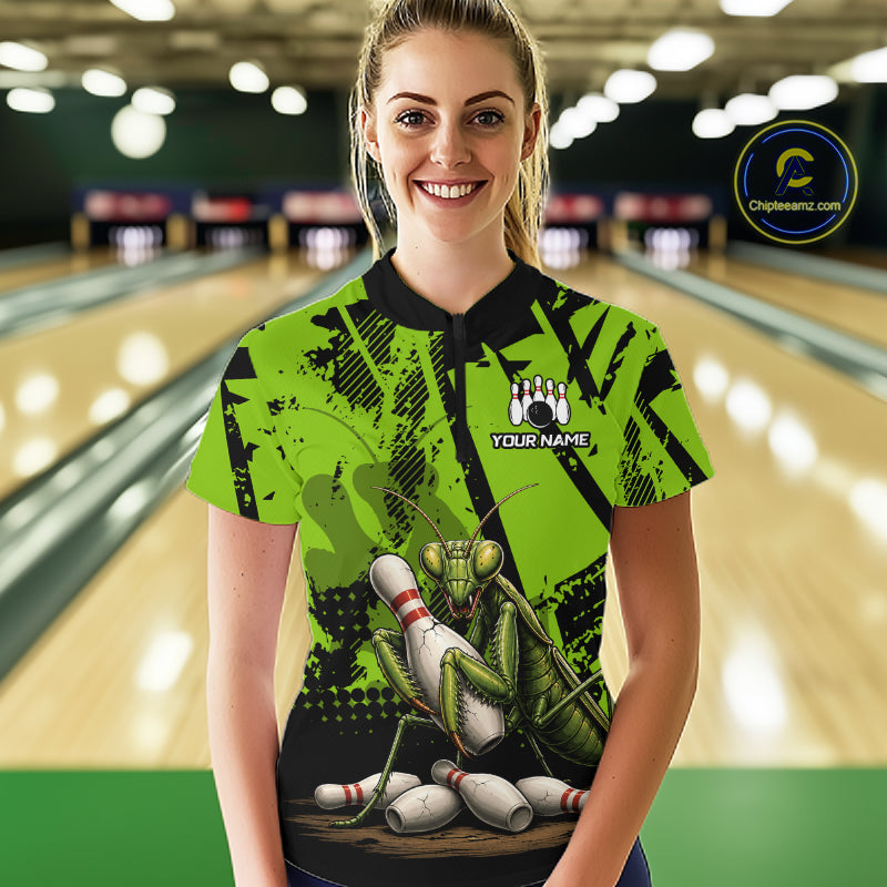 A woman stands in a bowling alley wearing a bright lime green and black short-sleeve bowling shirt with a cartoon praying mantis graphic and a custom name patch on the chest.