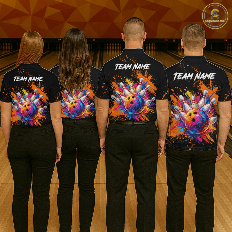 Four people standing in a bowling alley, viewed from behind, wearing matching black short-sleeve bowling shirts with colorful bowling ball and paint-splatter graphics on the back, plus white 'TEAM NAME' text.