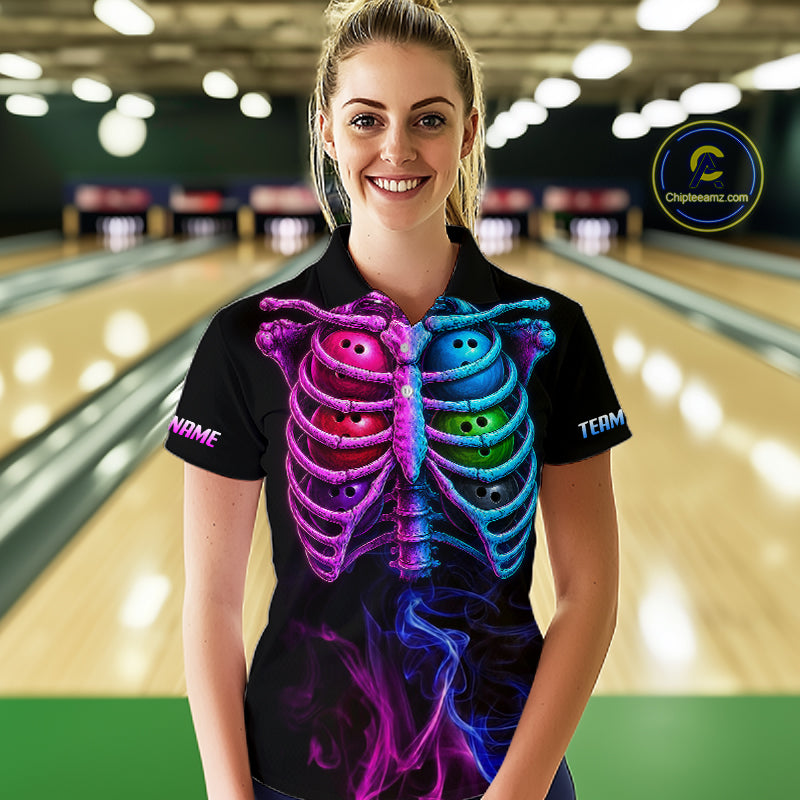 A woman wearing a black short-sleeve polo shirt with a vibrant neon rib cage graphic in pink, purple, blue, and green, standing in front of a blurred bowling alley background. 