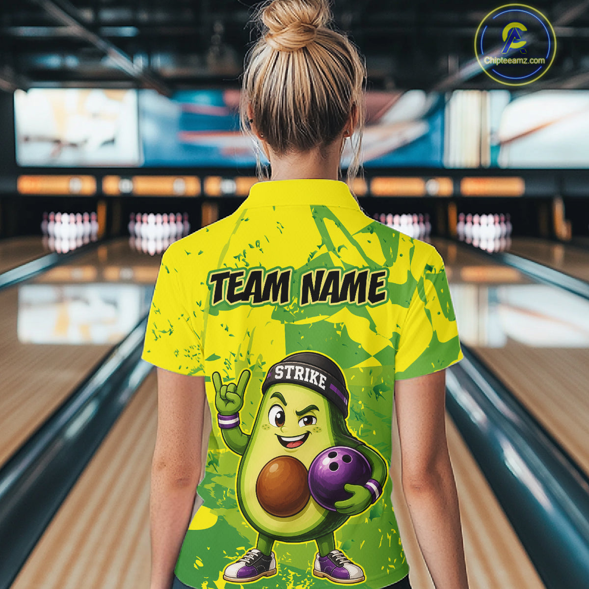 Person wearing a yellow bowling shirt with a cartoon avocado character in a bowling alley.