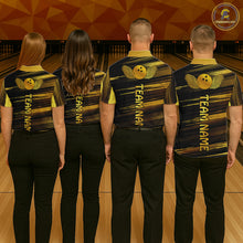 Load image into Gallery viewer, Group of four wearing custom black gold bowling shirts back view displaying personalized team names below a gold bowling ball emblem on a black gold brush stroke background at the bowling alley