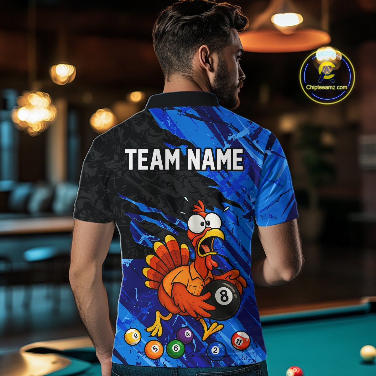 A man viewed from behind wearing a custom blue and black short-sleeve polo shirt with a cartoon turkey holding an 8-ball and the text 'TEAM NAME' on the back. The shirt is shown in a blurred pool hall environment