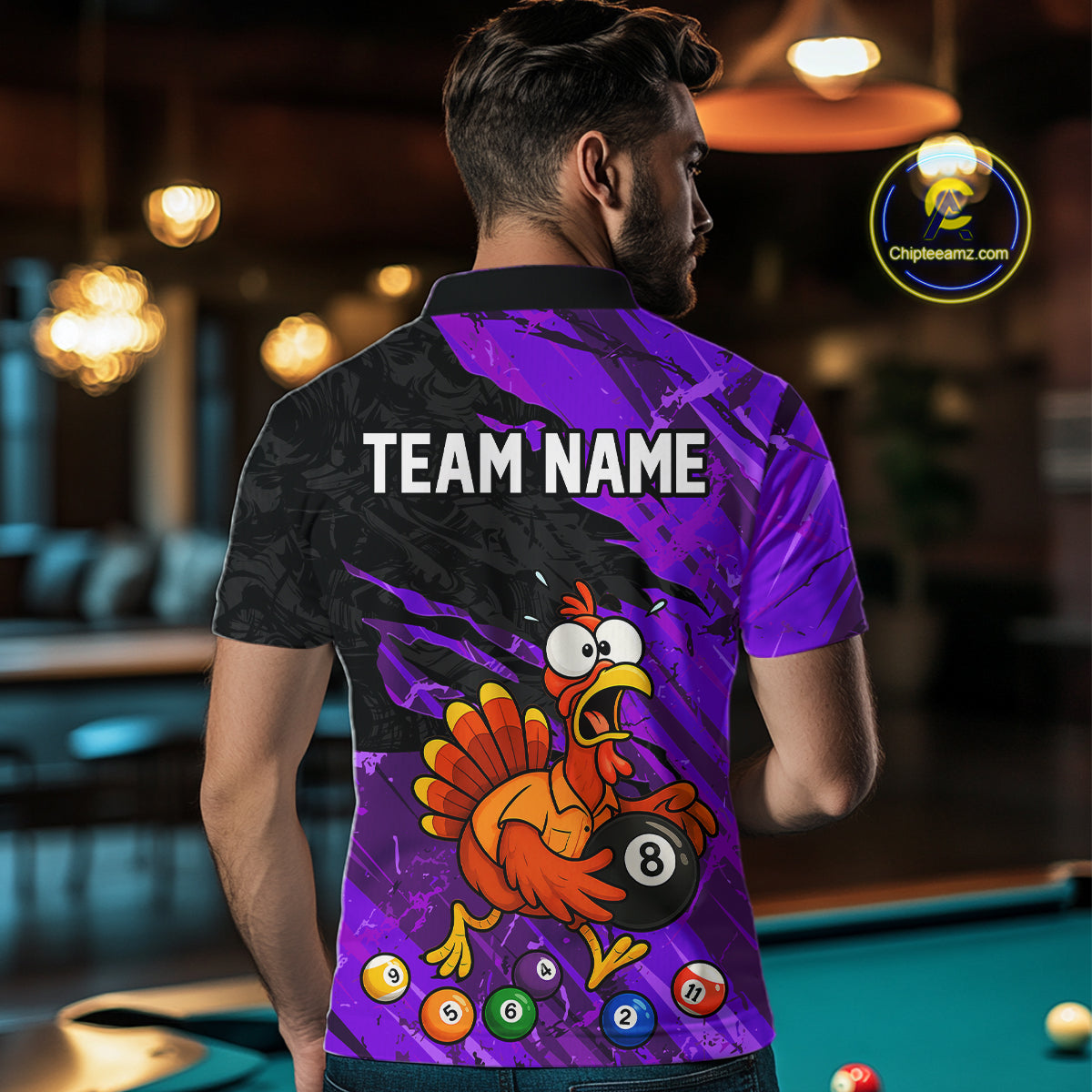 A man viewed from behind wearing a custom-printed short-sleeve polo shirt in a pool hall setting. The back of the shirt features a black and purple graphic background with a cartoon turkey holding an 8-ball pool bill, colorful pool balls, and the text 'TEAM NAME' in white.