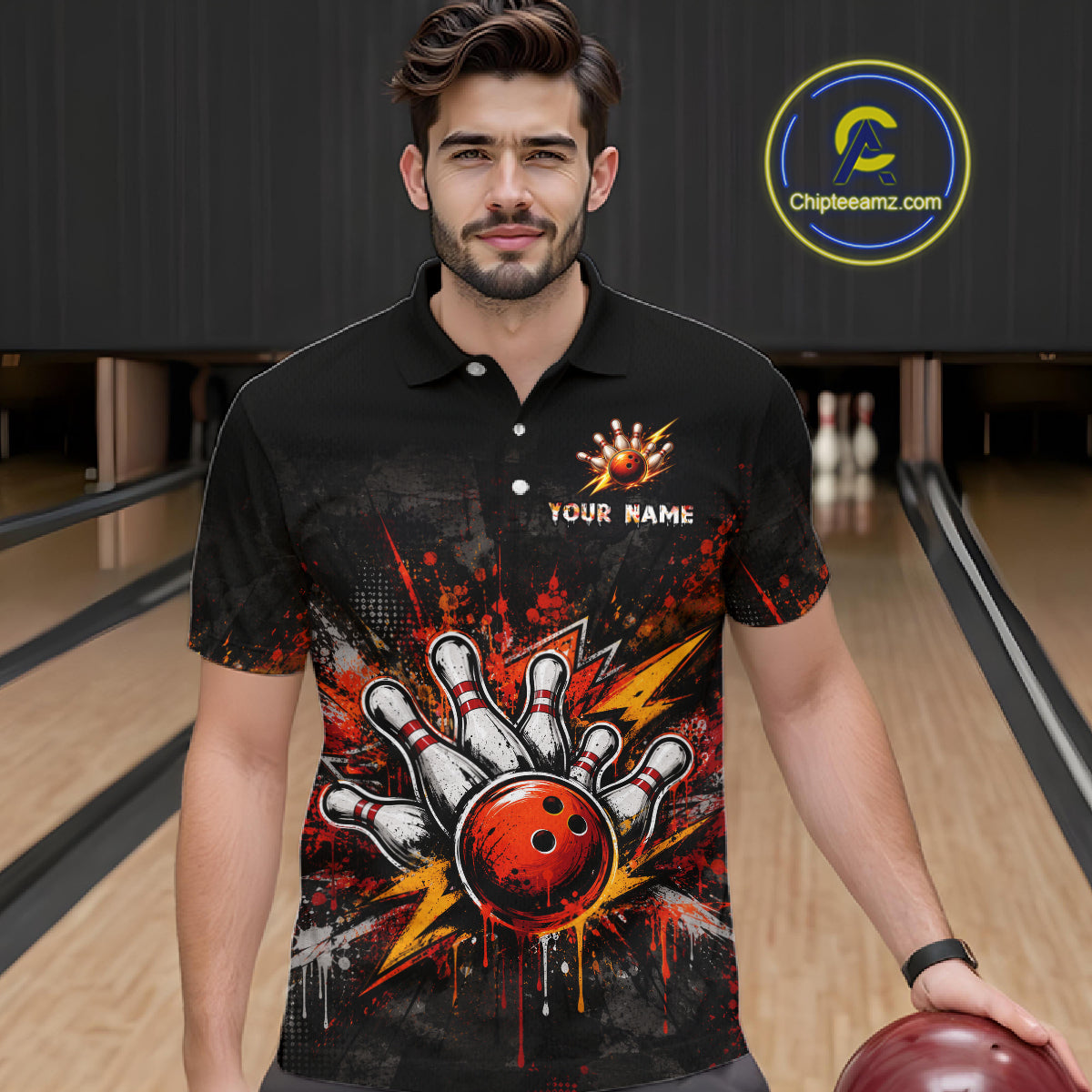 A man wearing a black short-sleeve bowling-themed polo shirt with a graphic of bowling pins, a red bowling ball, and paint splatters, standing in a bowling alley. 