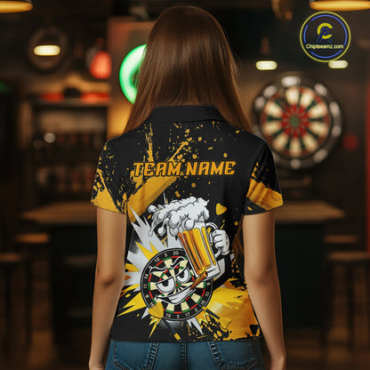 A woman viewed from behind wearing a black short-sleeve polo shirt with a large yellow, white, and gray graphic print on the back, featuring the text 'TEAM NAME' and a cartoon beer mug and dartboard design. The background is a dimly lit bar with dartboards and warm lighting.