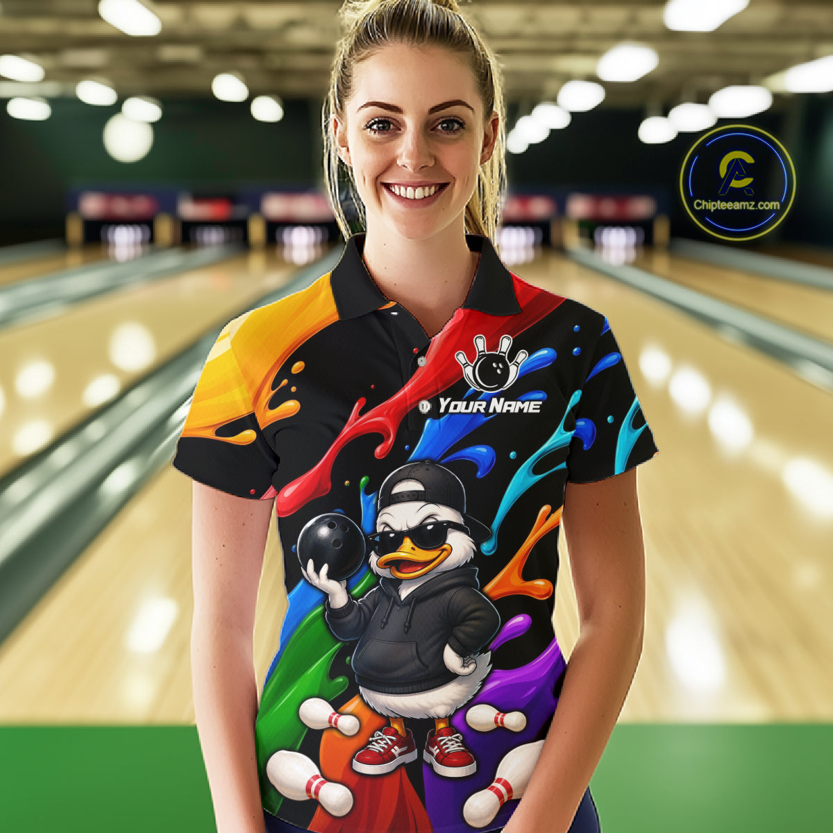 A woman wearing a colorful bowling-themed short-sleeve polo shirt with a cartoon duck graphic, standing in front of a blurred bowling alley background. 