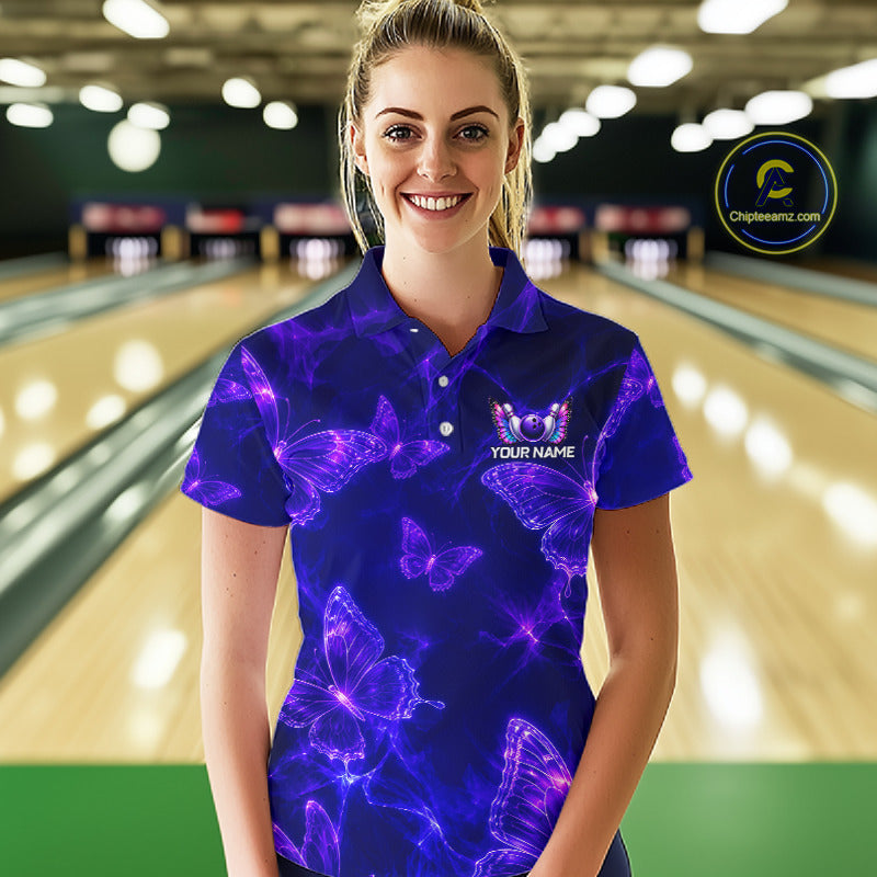 A woman stands in a bowling alley wearing a short-sleeve polo shirt with a vibrant purple and blue neon butterfly pattern. The shirt features a custom graphic with a butterfly, the text 'YOUR NAME'