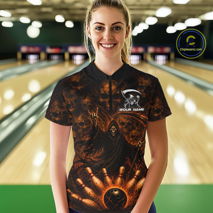 A woman standing in a bowling alley wearing a black short-sleeve bowling shirt with a fiery grim reaper graphic and a custom name printed on the chest. 