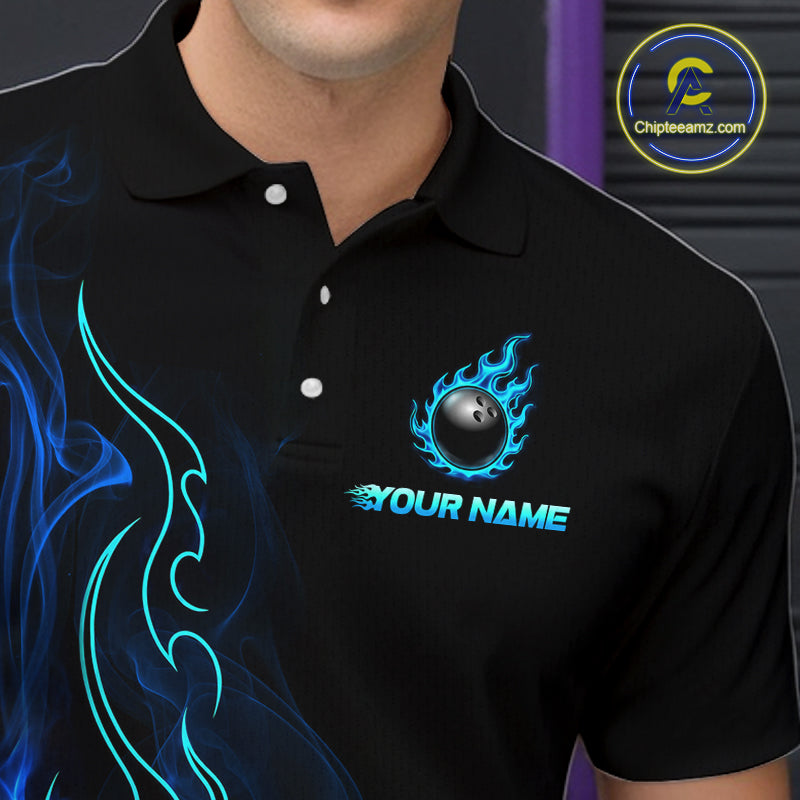 A close-up of a person wearing a black short-sleeve polo shirt with a custom bowling-themed chest graphic featuring a flaming bowling ball and the text 'YOUR NAME'. The shirt also has blue flame and tribal-style graphics on the left side.