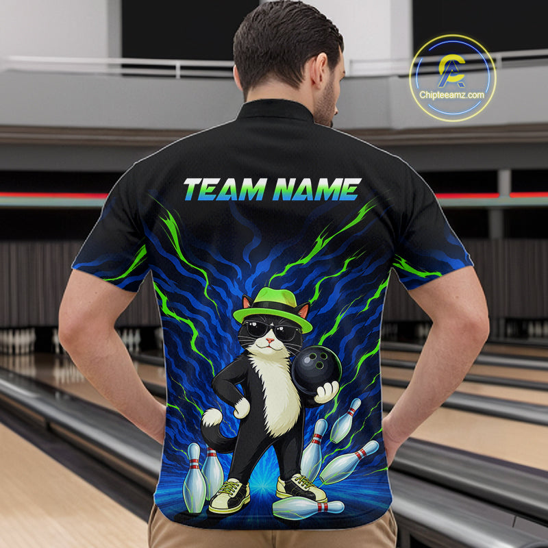 A man stands with his back to the camera in a bowling alley, wearing a black short-sleeve bowling shirt with a colorful graphic of a cat holding a bowling ball and the text 'TEAM NAME' across the upper back. Bowling lanes are visible in the background.