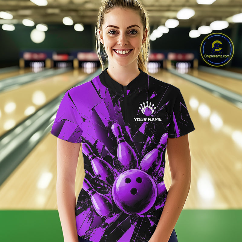 A woman wearing a custom bowling shirt with a purple and black bowling pin and ball graphic, standing in a bowling alley. The shirt features a black collar and a black upper chest with a purple bowling pin design, including pins and a bowling ball.