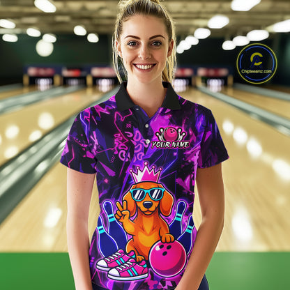 Woman wearing a black and purple bowling polo shirt featuring a cartoon dachshund wearing sunglasses and a crown, holding a pink bowling ball, with custom player name text.