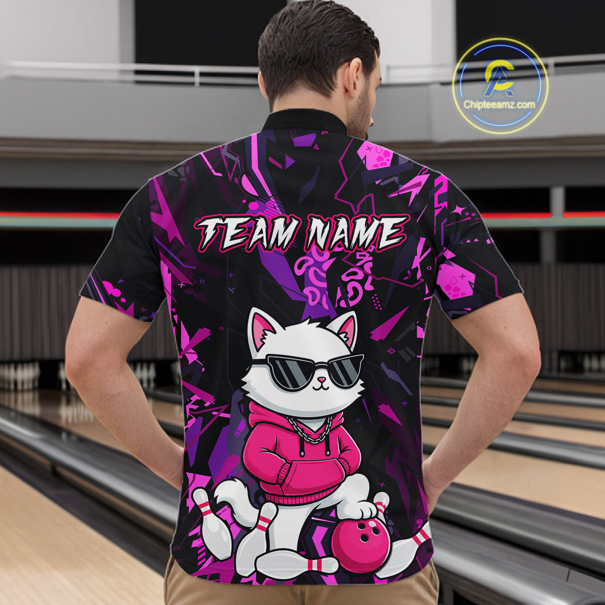 A man viewed from behind wearing a short-sleeve bowling-themed button-up shirt with a black and purple abstract background, a white cat wearing sunglasses and a pink hoodie, and the text 'TEAM NAME' across the upper back. Bowling lanes are visible in the background, and a 'ChipteeAmz'