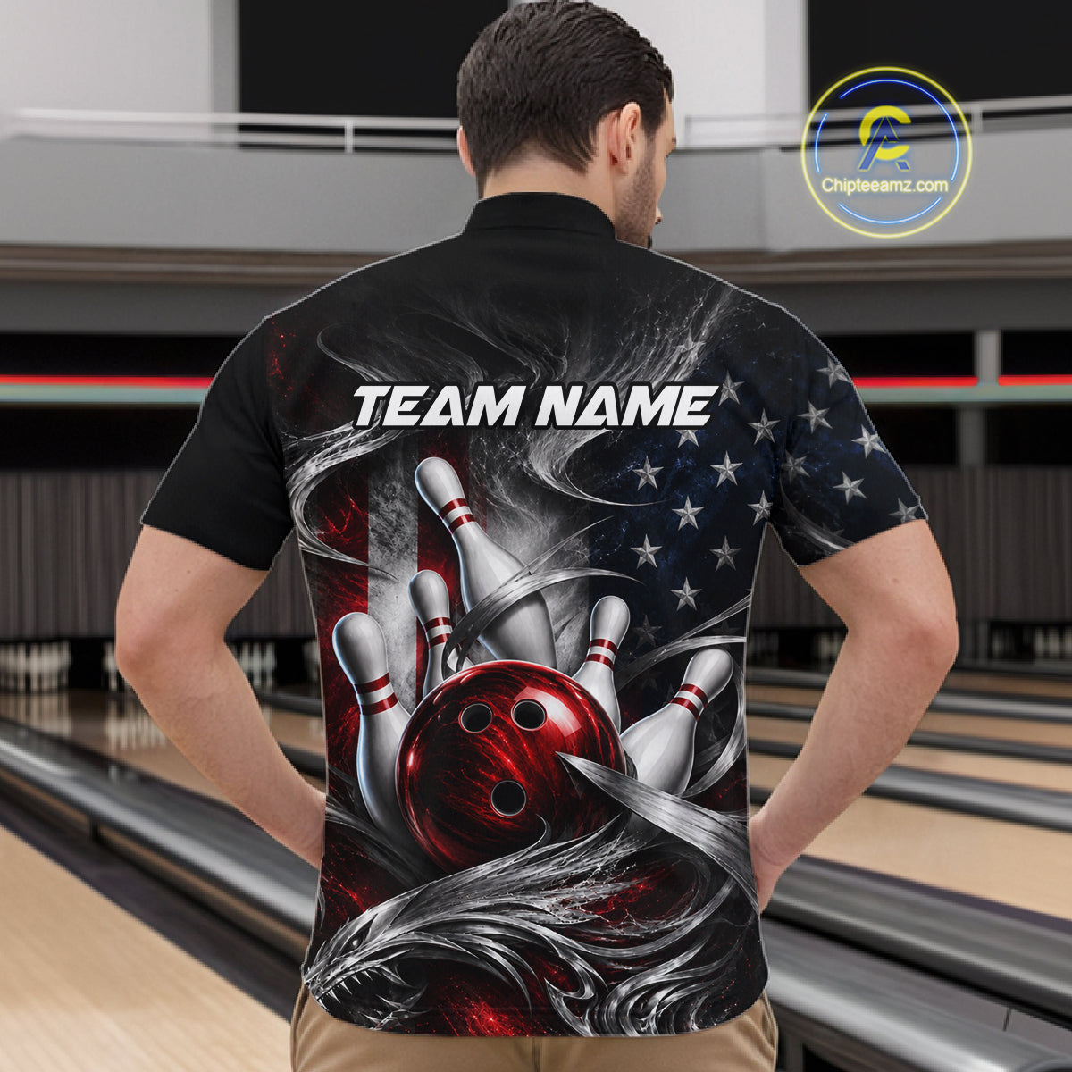 A man viewed from behind wearing a black short-sleeve bowling-themed shirt with a large graphic print of bowling pins, a red bowling ball, an American flag, and the text 'TEAM NAME'. The background shows bowling lanes in a bowling alley.