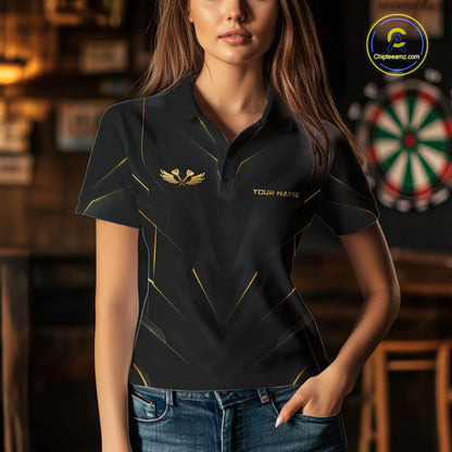 A woman wearing a black short-sleeve polo shirt with gold geometric line details and a gold winged emblem on the left chest, paired with blue jeans in a dimly lit indoor setting.