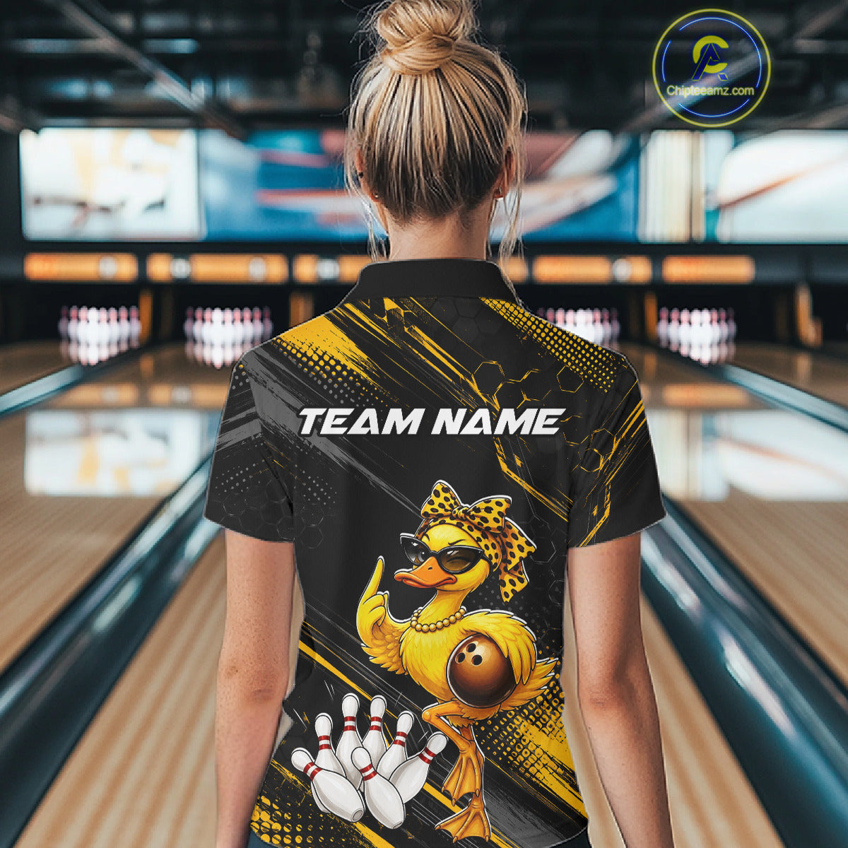 Person wearing a bowling shirt with a duck design and 'Team Name' text in a bowling alley.