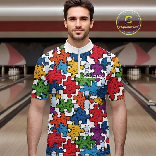 A man wearing a short-sleeve white quarter-zip bowling shirt with a colorful puzzle-piece pattern, standing in front of a bowling alley background. 