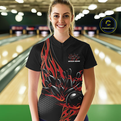 Female model front view inside bowling center wearing black quarter zip shirt featuring red flame bowling ball knocking down pins artwork