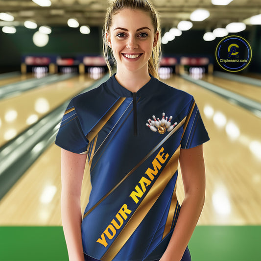 A woman wearing a custom bowling shirt stands in a bowling alley. The shirt is navy blue with gold diagonal stripes and the text 'YOUR NAME' printed on the front.