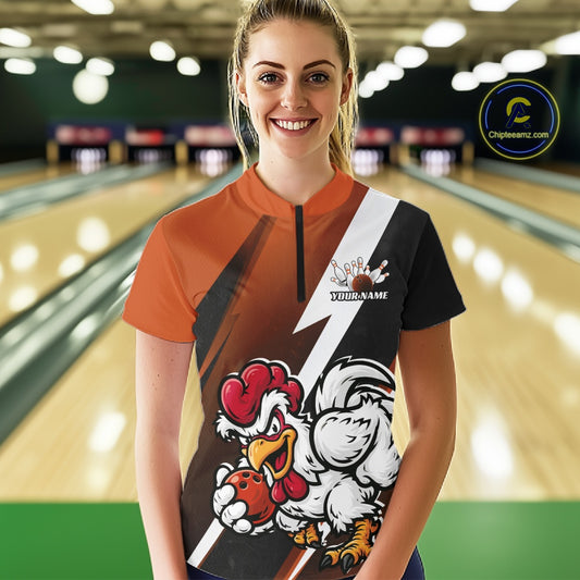 A woman standing in a bowling alley wearing a custom short-sleeve bowling jersey with an orange, black, and white design featuring a cartoon rooster mascot and the text 'Your Name'.