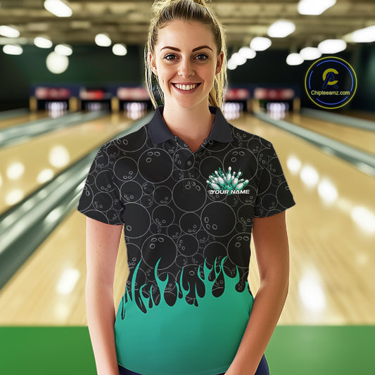 Front view of a female model in a bowling lane wearing a black polo shirt featuring bowling ball pattern with vibrant turquoise green flames rising from the bottom and dynamic flaming bowling graphics.