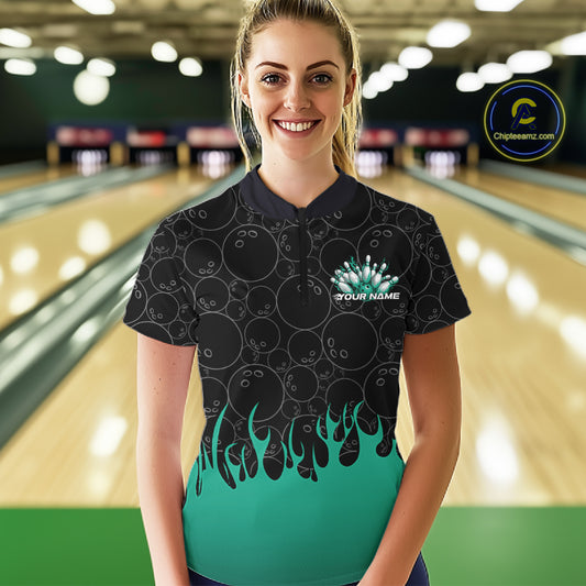 In a bowling lane, front view of a female model wearing a black bowling quarter-zip shirt with vibrant turquoise flames, showcasing flaming bowling ball action graphics.