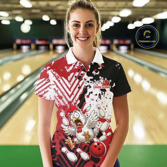 A woman stands in a bowling alley wearing a short-sleeve bowling-themed polo shirt with a red, white, and black splatter design, a cartoon chicken, bowling pins, and a red bowling ball graphic. The background shows blurred bowling lanes.
