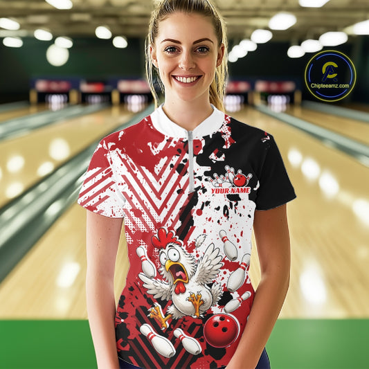 A woman standing in a bowling alley wearing a short-sleeve custom-printed bowling shirt with a red, white, and black splatter design, a cartoon rooster graphic, and a bowling ball illustration. The background shows blurred bowling lanes.