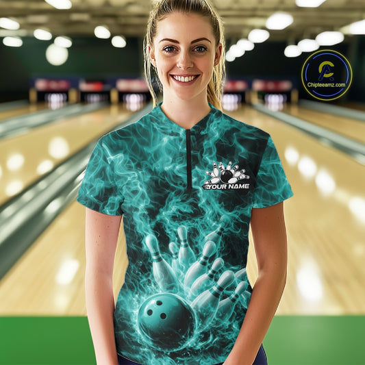Female model wearing a bowling quarter-zip in a bowling center with turquoise blue bowling ball artwork and fiery accents.