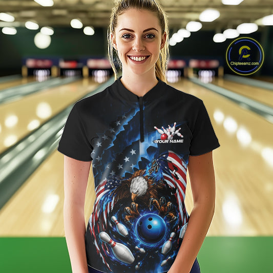 Female model front view in a bowling lane wearing a quarter zip shirt with bald eagle artwork, blue bowling ball, flying pins, and flag background.