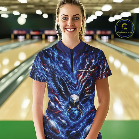 Front view female model at the bowling lane wearing a quarter zip shirt with eagle graphics, bowling ball, flowing flag accents, and pins.