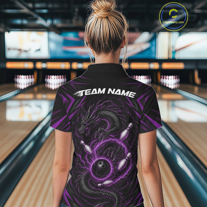 A woman viewed from behind wearing a black short-sleeve bowling polo shirt with a purple dragon and bowling pin graphic on the back, standing in a bowling alley. The shirt has 'TEAM NAME'across the upper back.