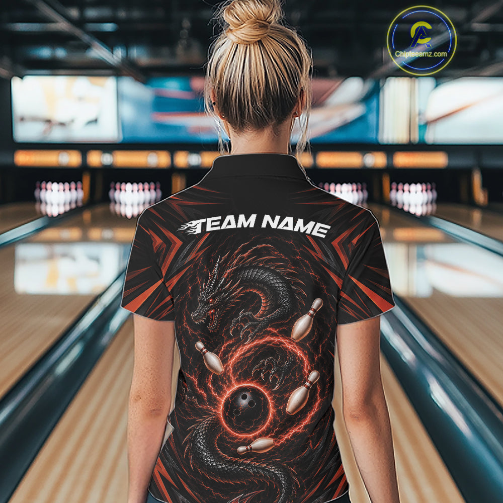 A woman viewed from behind wearing a black bowling-themed short-sleeve polo shirt with a orange and black dragon graphic and white 'TEAM NAME' text on the back, standing in a bowling alley.